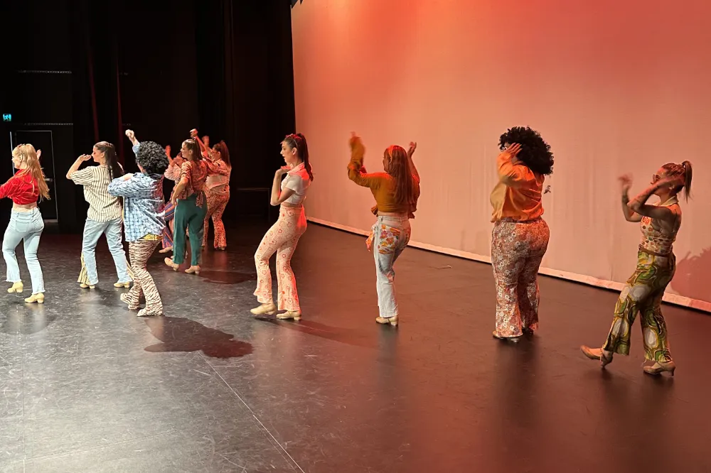 A line of women in all different types of clothing walking and dancing.
